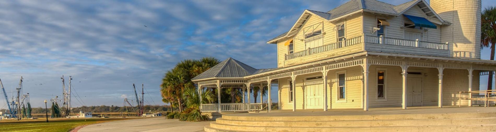 Two-story house by a river under a cloudy blue sky.