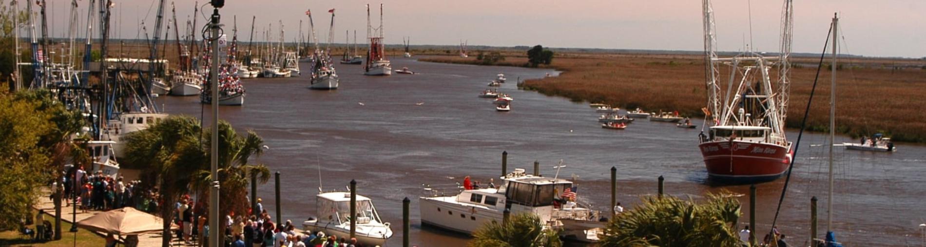 Boats on a calm river with grassy banks and a distant marshland background.