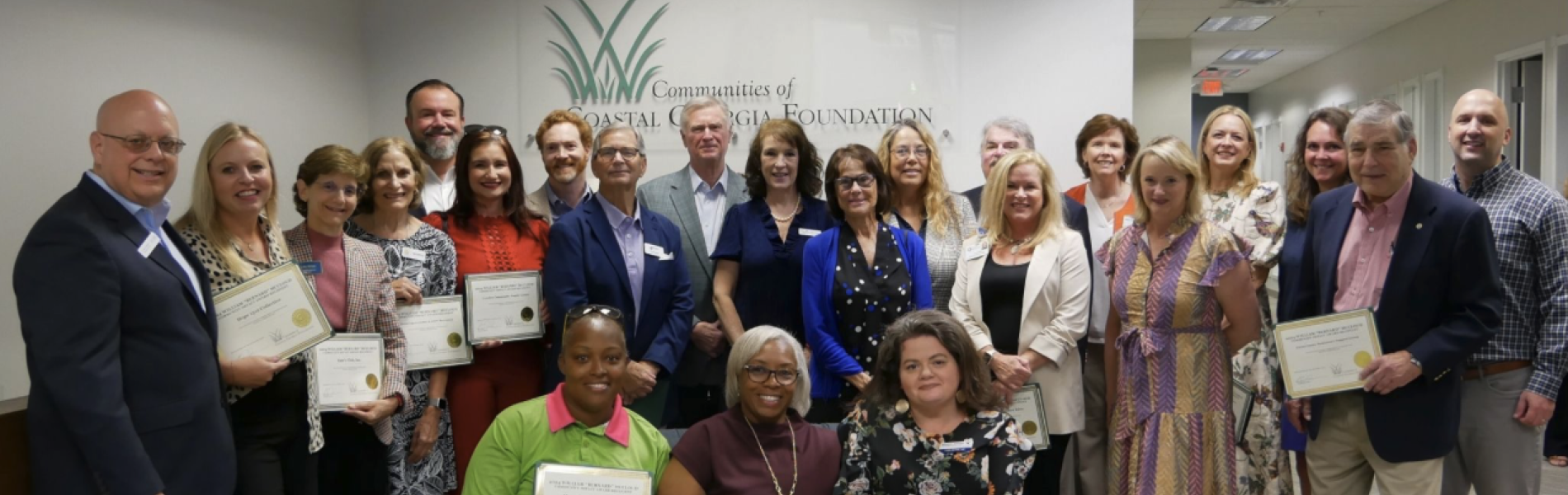 Group of award recipients smiling, holding certificates indoors.