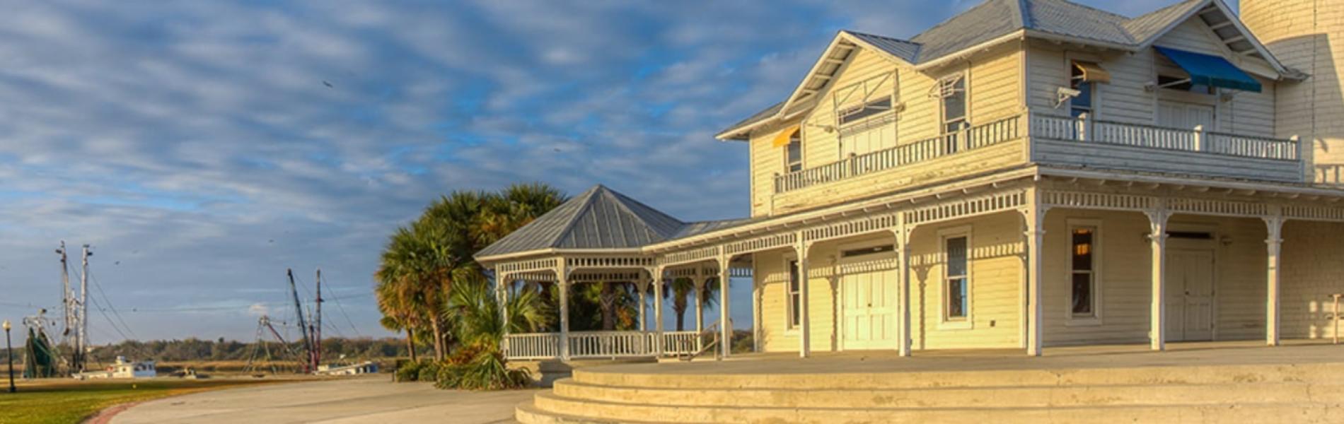 Two-story house by a river under a cloudy blue sky.